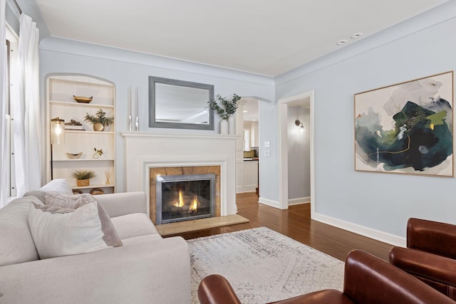 living room featuring built in features, a tile fireplace, baseboards, and dark wood-style flooring