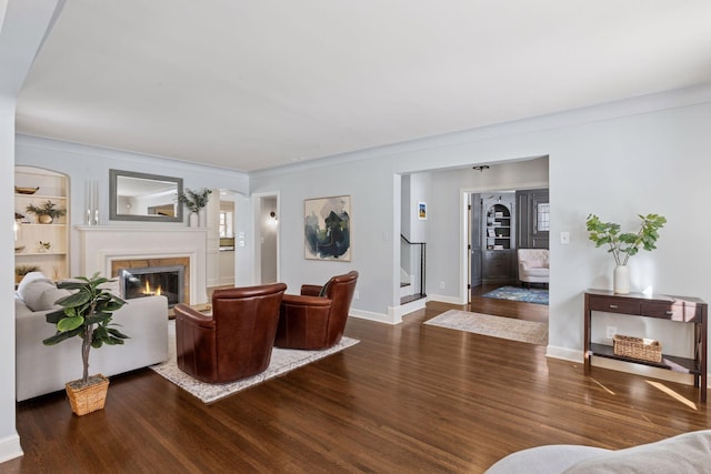 living area with a glass covered fireplace, stairway, baseboards, and wood finished floors