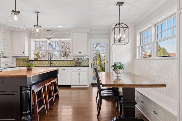 kitchen featuring dark wood-type flooring, butcher block countertops, white cabinetry, crown molding, and decorative backsplash