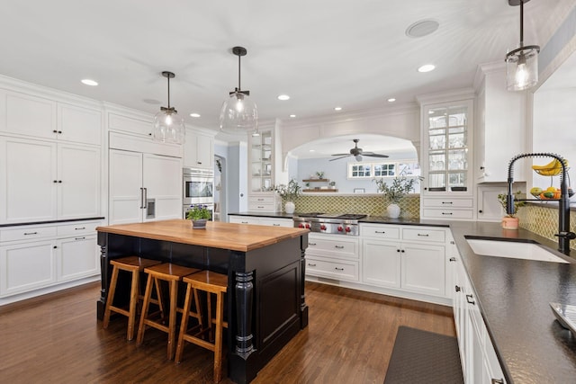 kitchen with a sink, arched walkways, white cabinets, butcher block counters, and glass insert cabinets