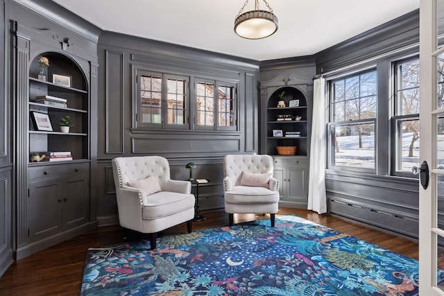 living area with a decorative wall, built in features, and dark wood-type flooring