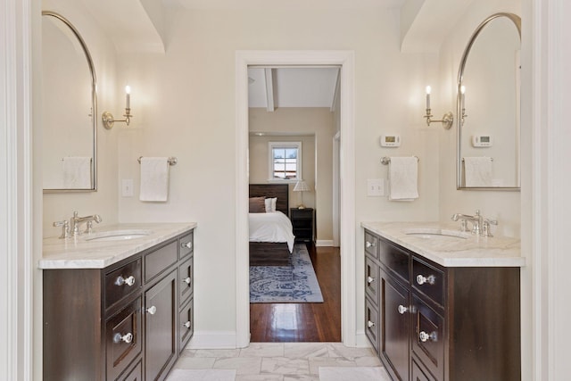 bathroom featuring a sink, baseboards, two vanities, and ensuite bathroom