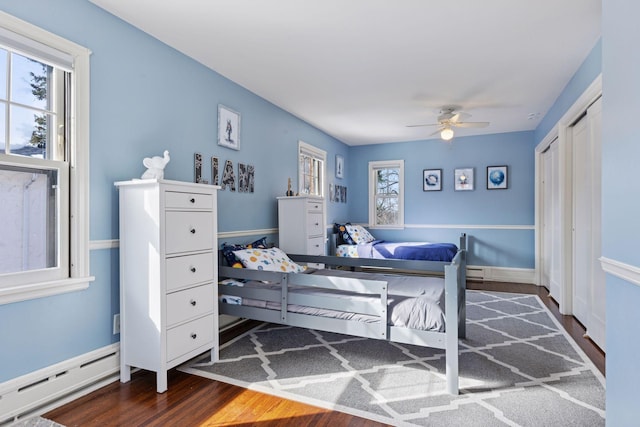 bedroom with wood finished floors, baseboard heating, and ceiling fan