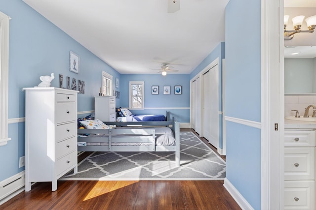 bedroom with a ceiling fan, a sink, a baseboard heating unit, wood finished floors, and a closet