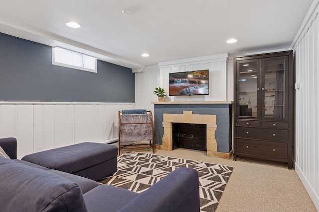 living area with recessed lighting, carpet, a stone fireplace, and wainscoting