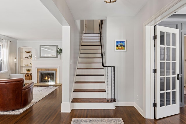 stairs featuring a glass covered fireplace, built in features, wood finished floors, and baseboards