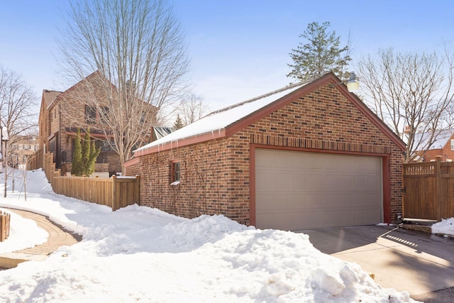 view of snow covered exterior featuring a garage, fence, brick siding, and a chimney