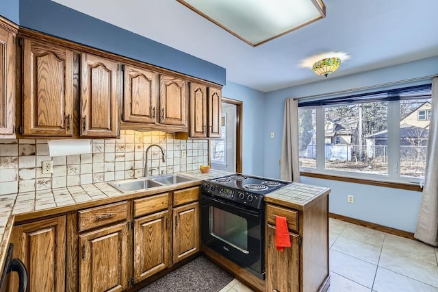 kitchen with electric range, a sink, backsplash, a peninsula, and tile counters