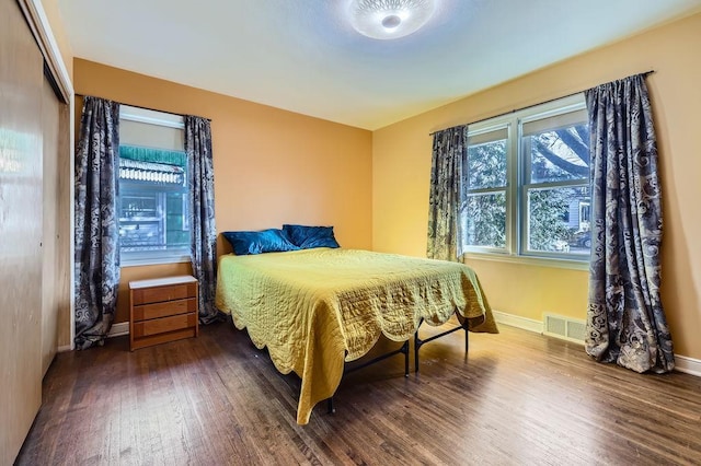 bedroom with wood finished floors, visible vents, a closet, and baseboards