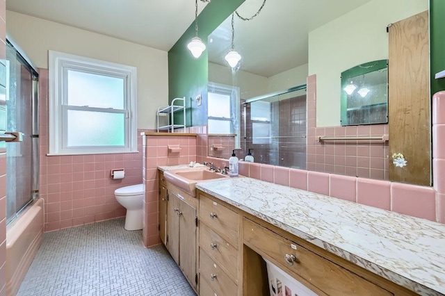 full bath with bath / shower combo with glass door, toilet, vanity, tile patterned floors, and tile walls