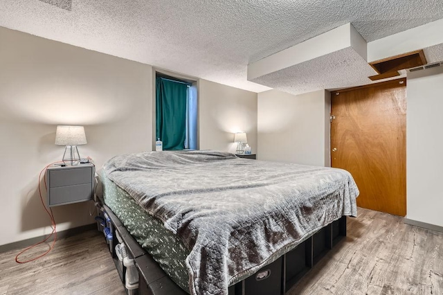 bedroom with visible vents, wood finished floors, baseboards, and a textured ceiling