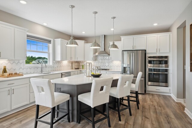 kitchen with a breakfast bar area, appliances with stainless steel finishes, white cabinets, wall chimney exhaust hood, and a sink