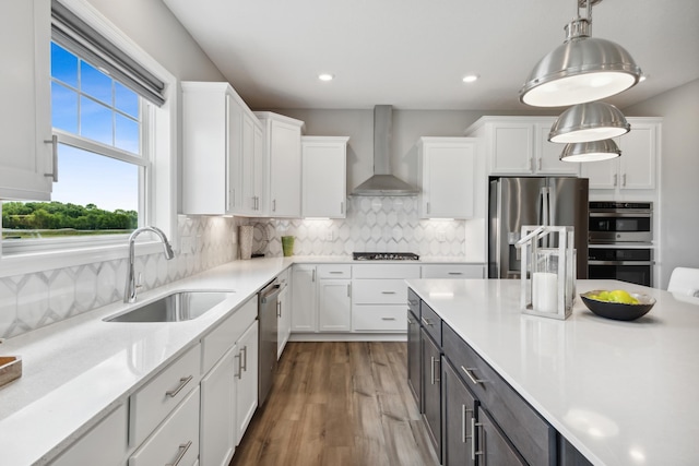 kitchen featuring a sink, wall chimney range hood, white cabinetry, and stainless steel appliances