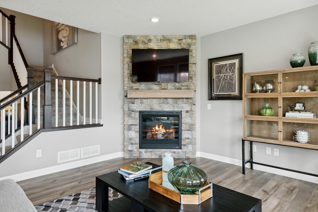 living room with stairway, wood finished floors, visible vents, baseboards, and a stone fireplace