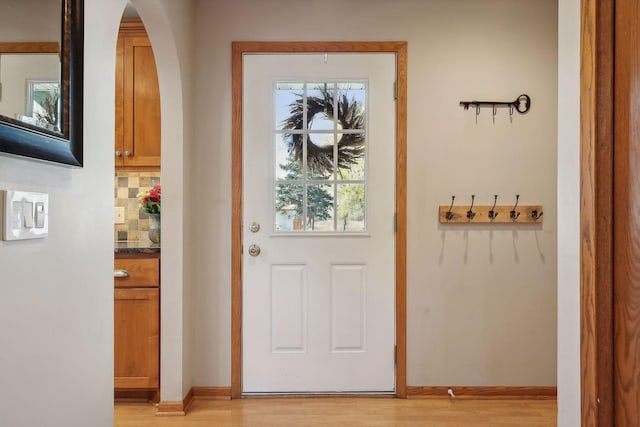 doorway with arched walkways, light wood finished floors, and baseboards