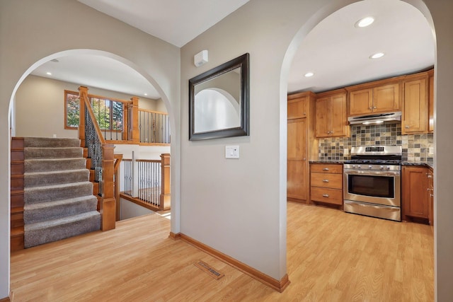 kitchen with visible vents, light wood-style flooring, decorative backsplash, under cabinet range hood, and gas range