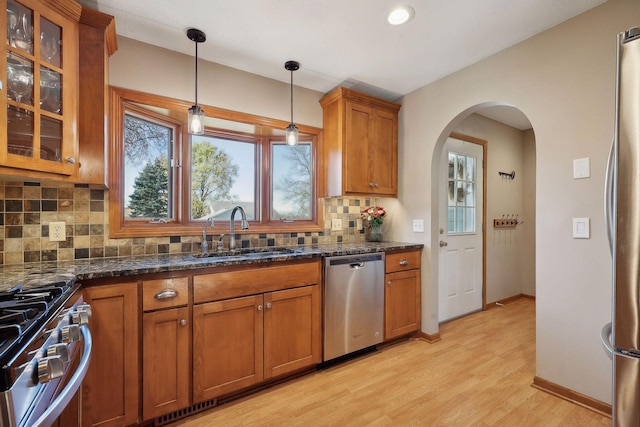 kitchen with hanging light fixtures, brown cabinets, appliances with stainless steel finishes, arched walkways, and a sink