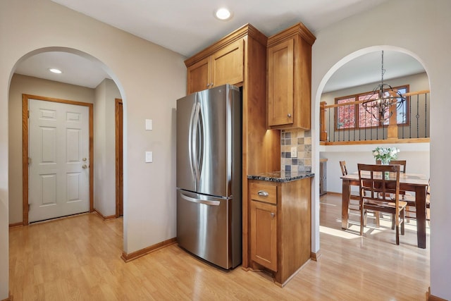 kitchen featuring dark stone countertops, brown cabinetry, light wood-type flooring, freestanding refrigerator, and tasteful backsplash