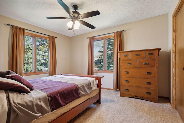 bedroom with ceiling fan, light colored carpet, baseboards, and a textured ceiling