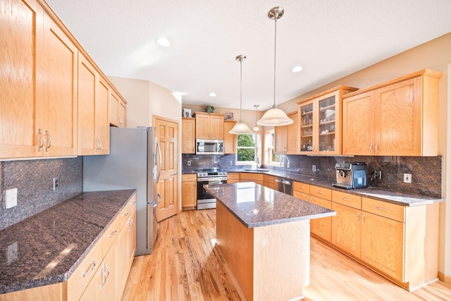 kitchen with light wood-style flooring, glass insert cabinets, a kitchen island, and stainless steel appliances