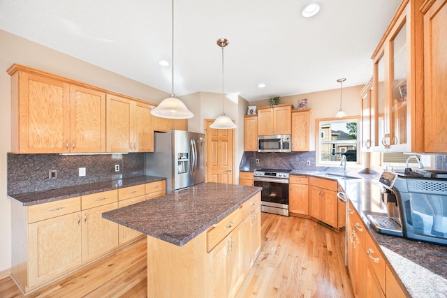 kitchen featuring a kitchen island, decorative backsplash, appliances with stainless steel finishes, light wood-style floors, and a sink