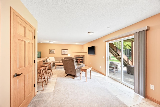 living area with a textured ceiling, light tile patterned floors, baseboards, and a lit fireplace