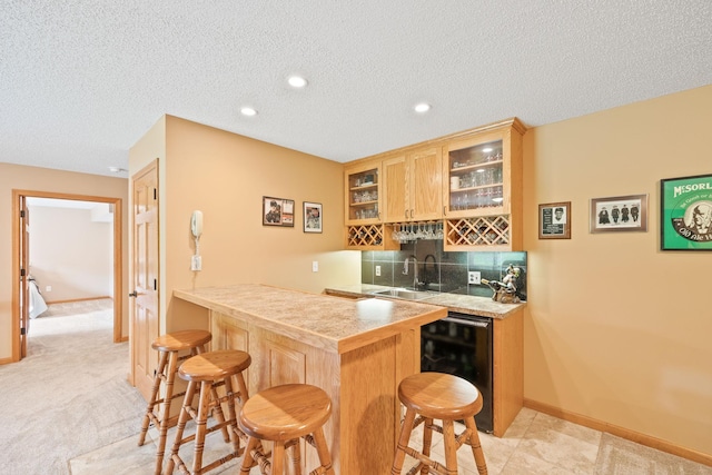 kitchen with backsplash, glass insert cabinets, beverage cooler, a breakfast bar, and a peninsula