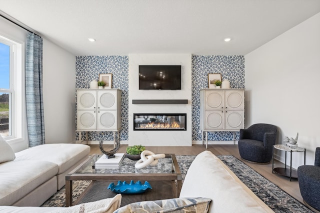 living room with a glass covered fireplace, wallpapered walls, and an accent wall