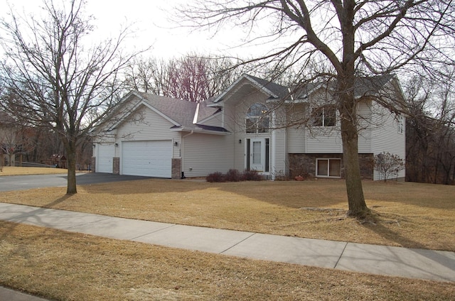 split level home featuring aphalt driveway, a garage, a front yard, and a shingled roof