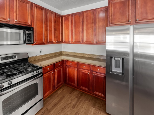 kitchen featuring stainless steel appliances, reddish brown cabinets, a textured ceiling, and wood finished floors