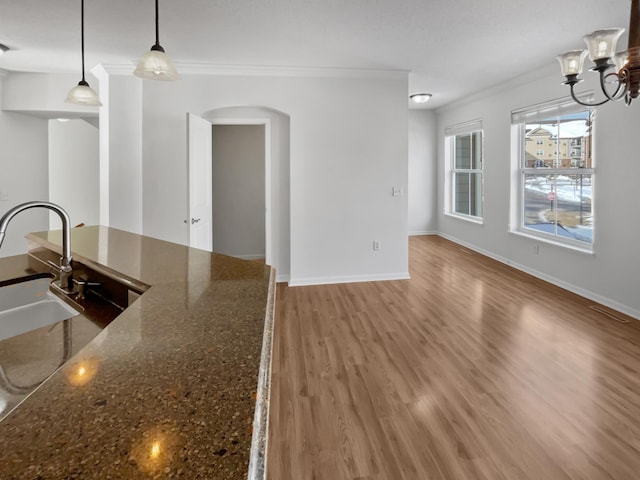 kitchen featuring baseboards, arched walkways, wood finished floors, and crown molding