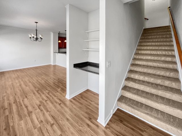 stairway featuring baseboards, a notable chandelier, and wood finished floors