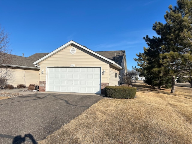 view of property exterior featuring brick siding, an attached garage, aphalt driveway, and a yard