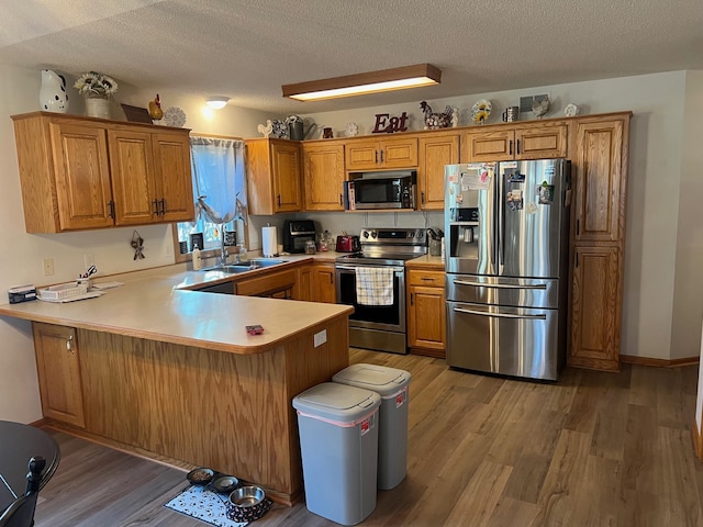 kitchen with brown cabinetry, a peninsula, stainless steel appliances, light wood-style floors, and a textured ceiling