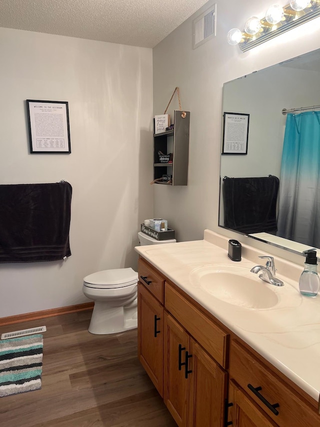 full bath with visible vents, toilet, vanity, wood finished floors, and a textured ceiling