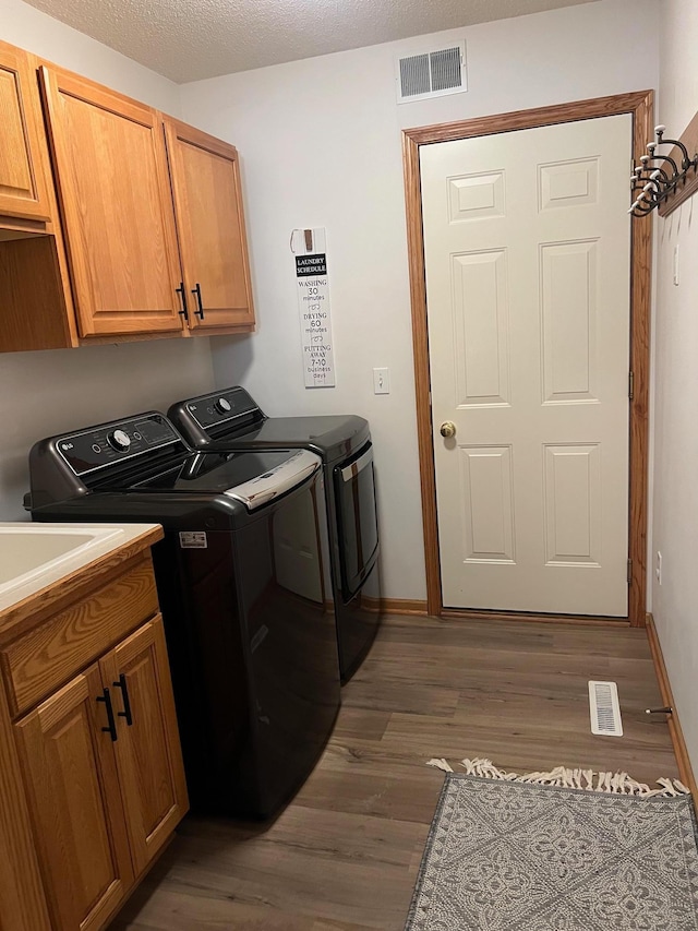 laundry area featuring visible vents, cabinet space, dark wood-type flooring, and washing machine and dryer