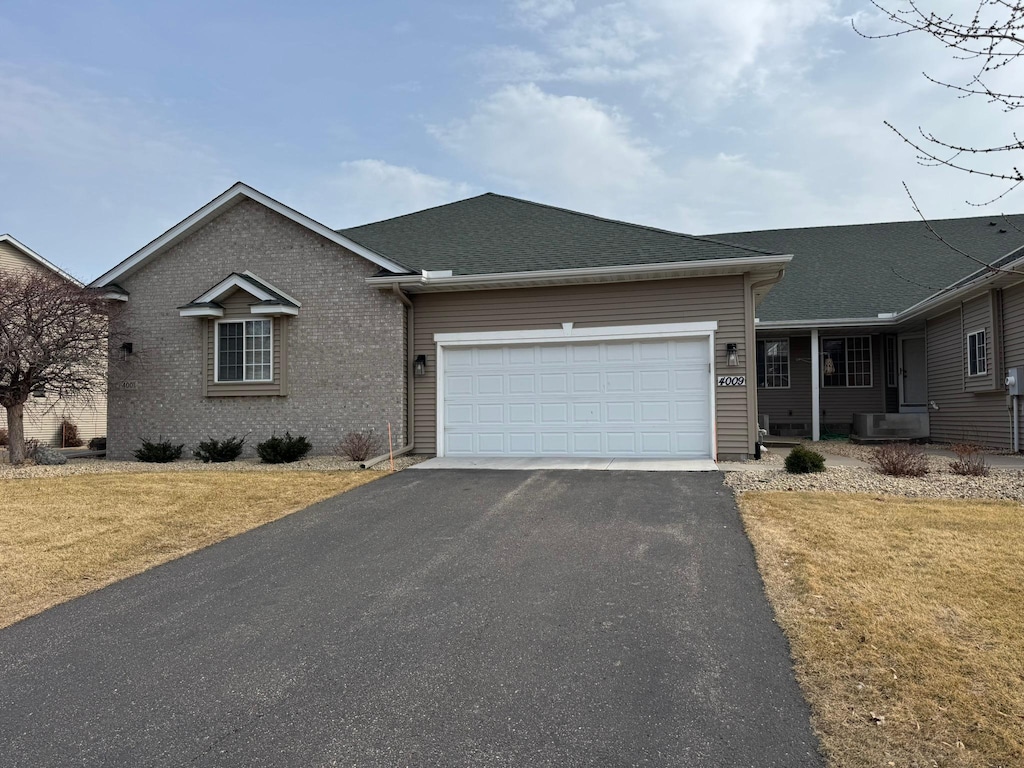 ranch-style home featuring aphalt driveway, a garage, a front yard, and roof with shingles