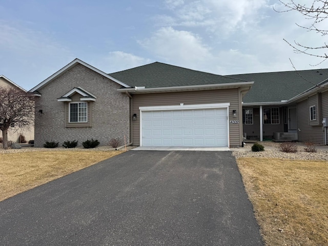 ranch-style house featuring driveway, a front lawn, a garage, and roof with shingles