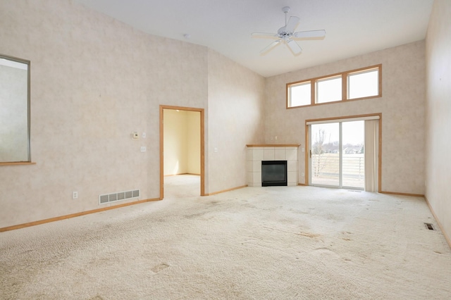 unfurnished living room with visible vents, a towering ceiling, carpet flooring, ceiling fan, and a tile fireplace