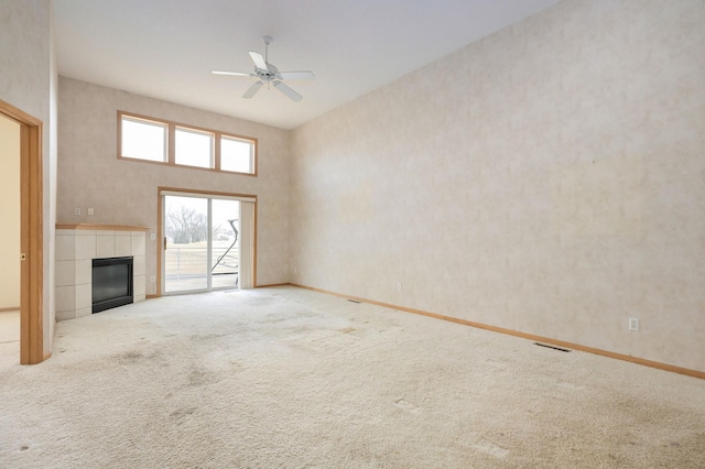 unfurnished living room featuring a ceiling fan, baseboards, carpet floors, a high ceiling, and a fireplace