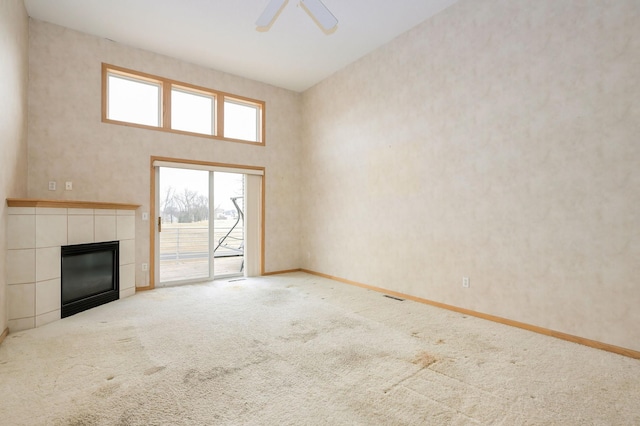 unfurnished living room featuring a ceiling fan, baseboards, a fireplace, a towering ceiling, and carpet flooring