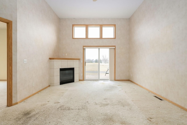 unfurnished living room featuring visible vents, baseboards, carpet floors, a high ceiling, and a tile fireplace