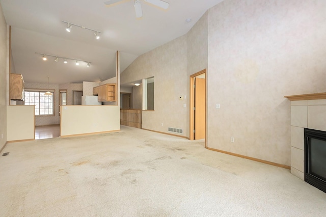 unfurnished living room featuring a ceiling fan, visible vents, track lighting, a tiled fireplace, and carpet flooring