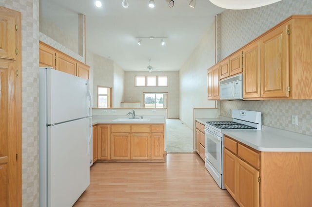 kitchen with white appliances, wallpapered walls, a peninsula, ceiling fan, and a sink