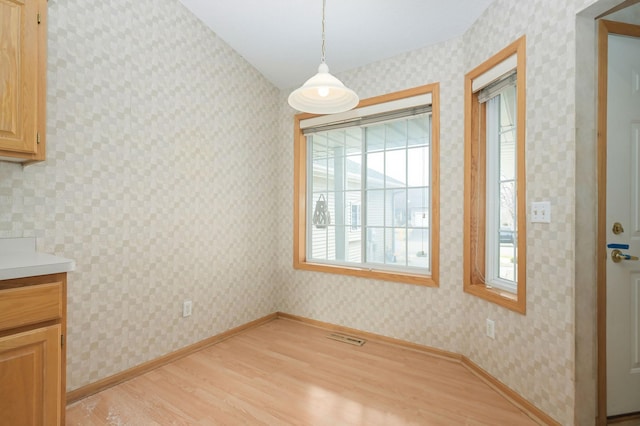 unfurnished dining area featuring light wood finished floors, visible vents, wallpapered walls, and baseboards