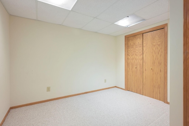 unfurnished bedroom with a paneled ceiling, a closet, baseboards, and carpet