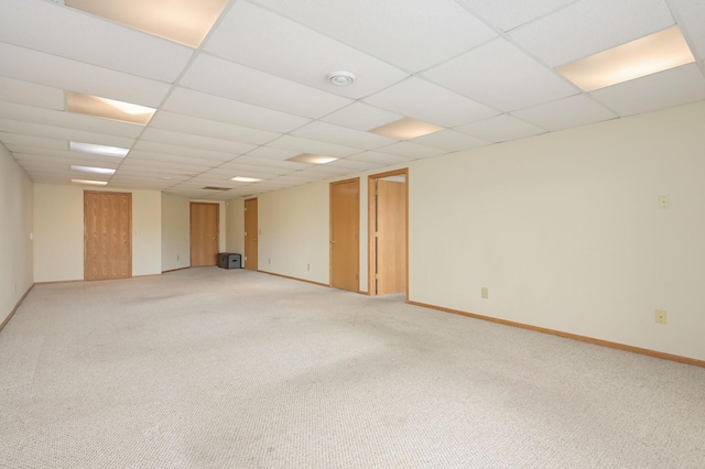 empty room with a drop ceiling, baseboards, and light colored carpet