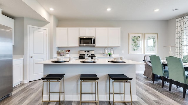 kitchen with a breakfast bar, stainless steel appliances, light wood-style floors, white cabinets, and light countertops