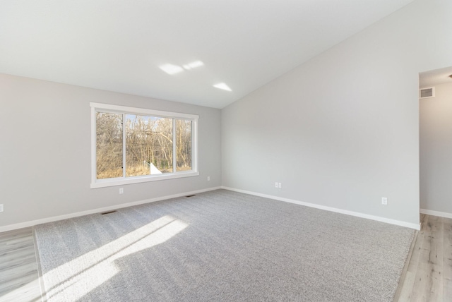 spare room featuring visible vents, lofted ceiling, baseboards, and light wood finished floors