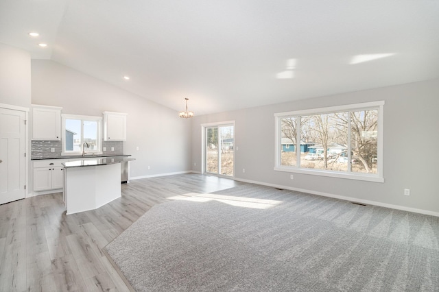 living area with baseboards, light wood finished floors, high vaulted ceiling, an inviting chandelier, and recessed lighting